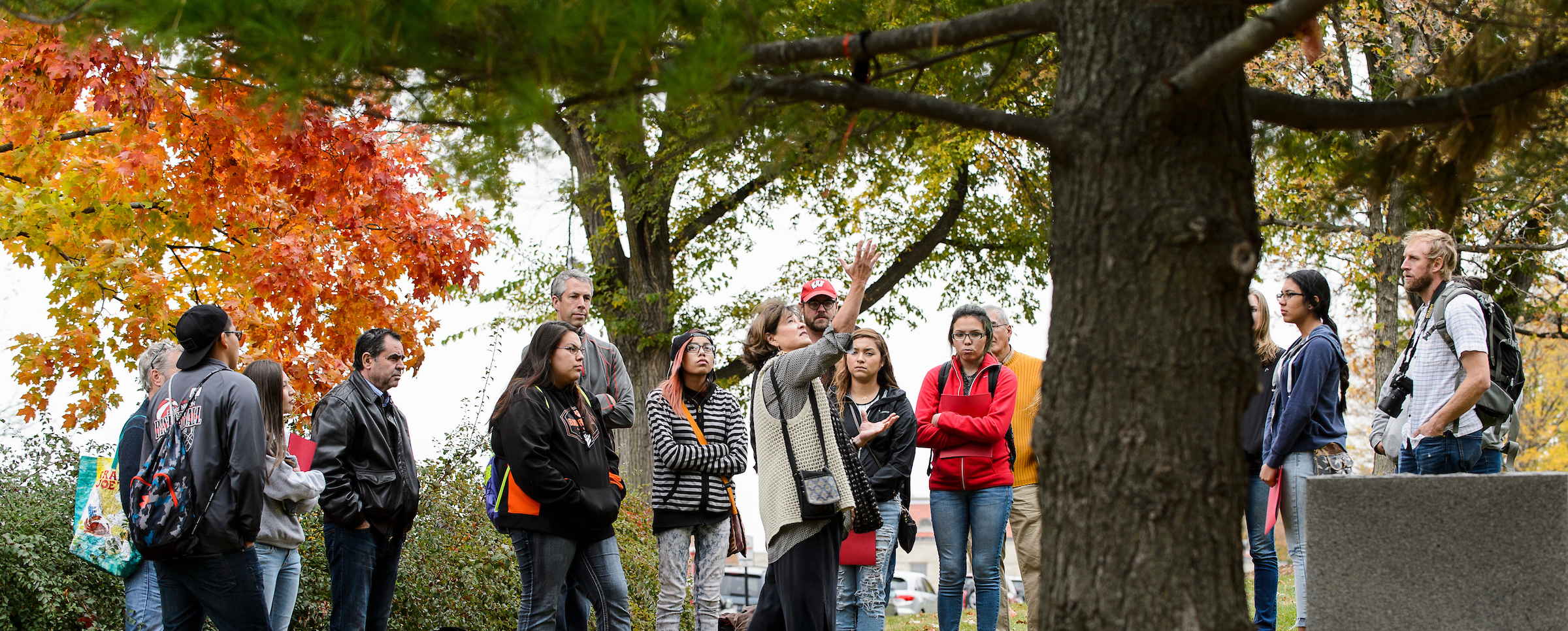 Patty Loew (wearing white sweater vest at center), professor of life sciences communication and a Bad River tribal member, talks about cultural history and digital storytelling with nine high school students from Wisconsin's Ho-Chunk Nation as the youth gathered near a Native American effigy mound and the Tree of Peace on Observatory Hill at the University of Wisconsin-Madison during autumn on Oct. 23, 2015. The UW Arboretum's Earth Partnership Program and UW-Madison's Nelson Institute for Environmental Studies hosted the group's one-day visit to campus. (Photo by Jeff Miller/UW-Madison)